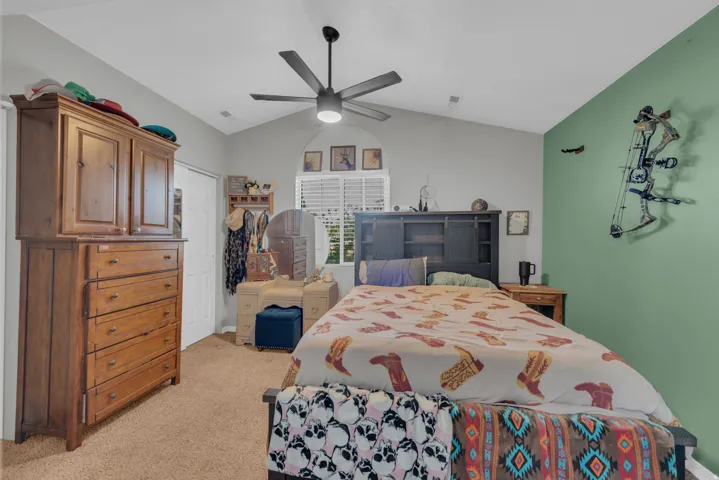 Vaulted ceiling with a ceiling fan, arched window with horizontal blinds, and carpeted flooring