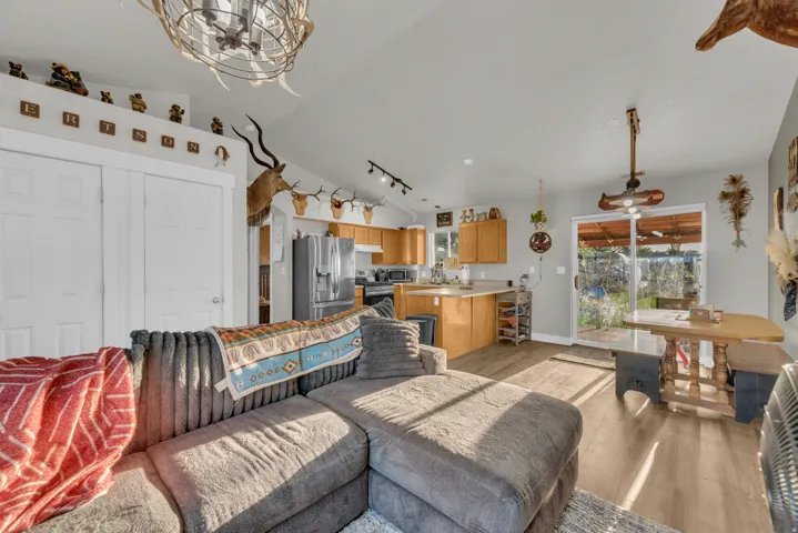 Vaulted ceilings, wood-finish flooring, kitchen with light wood cabinetry, stainless steel refrigerator, and glass sliding door