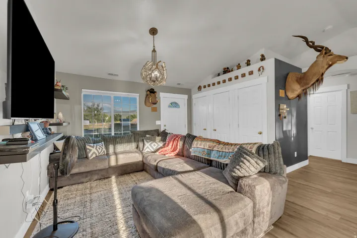 Vaulted ceiling, light wood-finish flooring, white panel doors, modern chandelier, and large windows