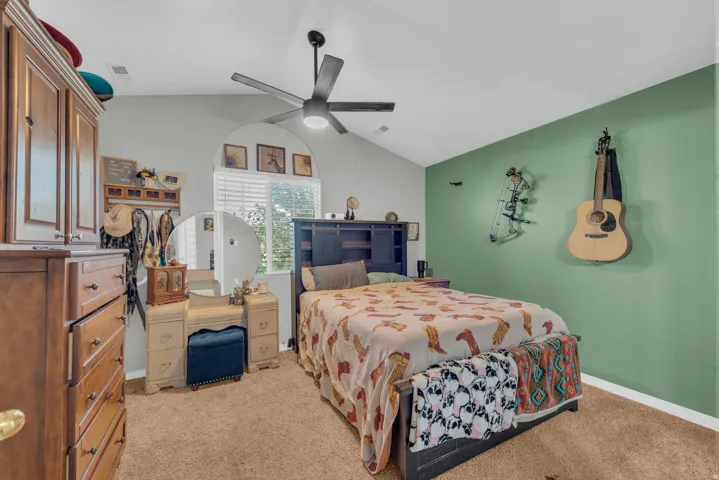 Vaulted ceiling with a ceiling fan, arched window with blinds, and carpeted flooring