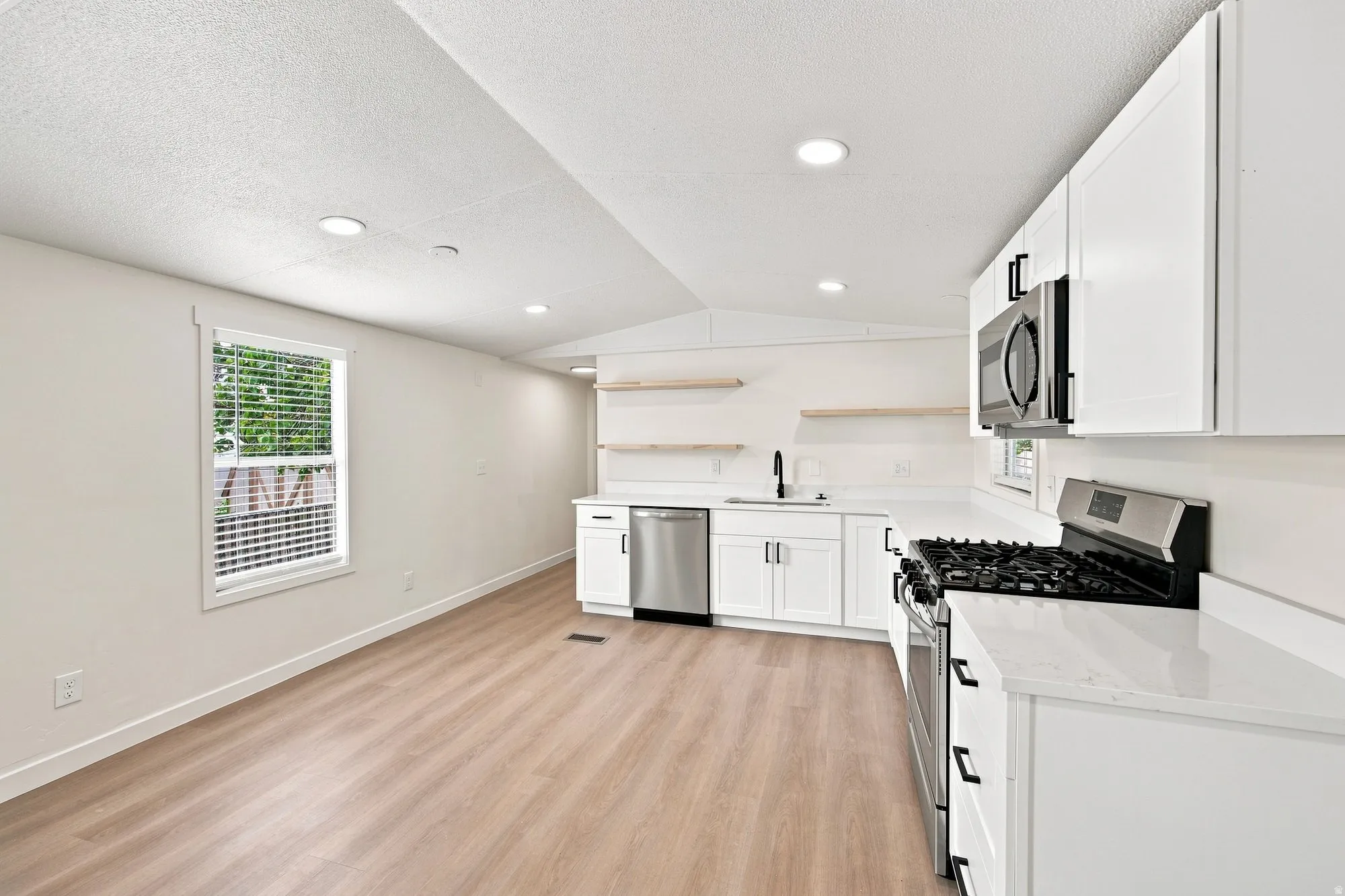 Modern kitchen featuring stainless steel appliances, white cabinetry, integrated sink with matte black fixtures, recessed lighting, and wood-finish flooring