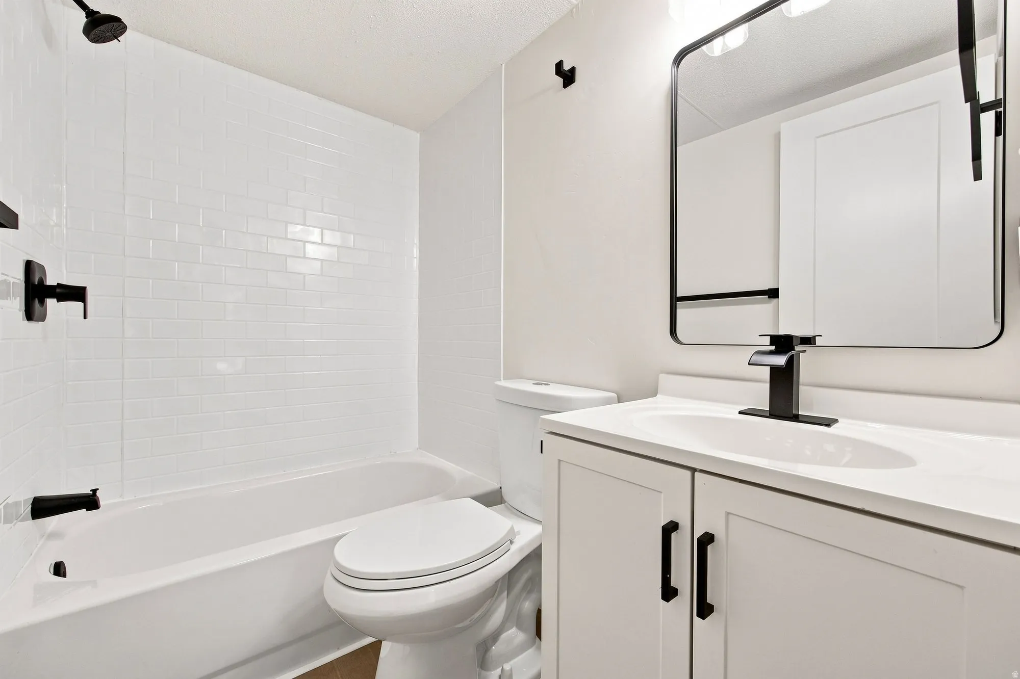 White subway tile surround, matte black fixtures, white vanity with integrated sink, white countertop, and framed mirror
