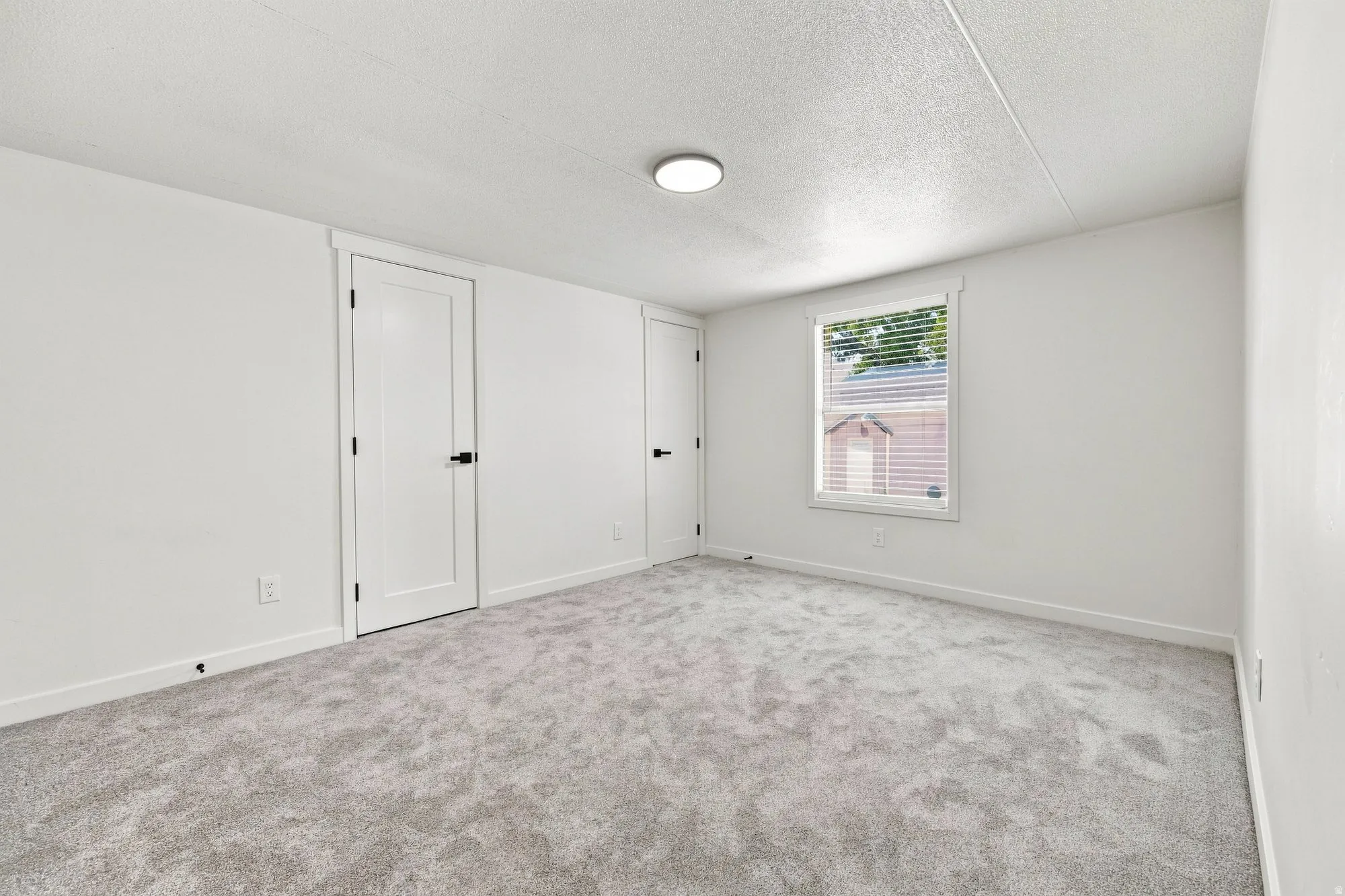 Neutral tone carpeting, white walls, and a window with blinds