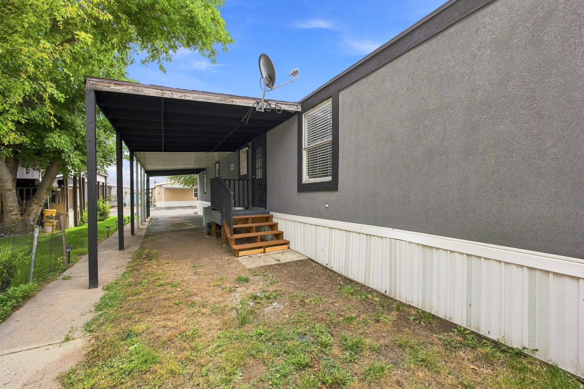 Covered walkway leading to a porch with wood steps and railing, featuring a stucco-finish exterior