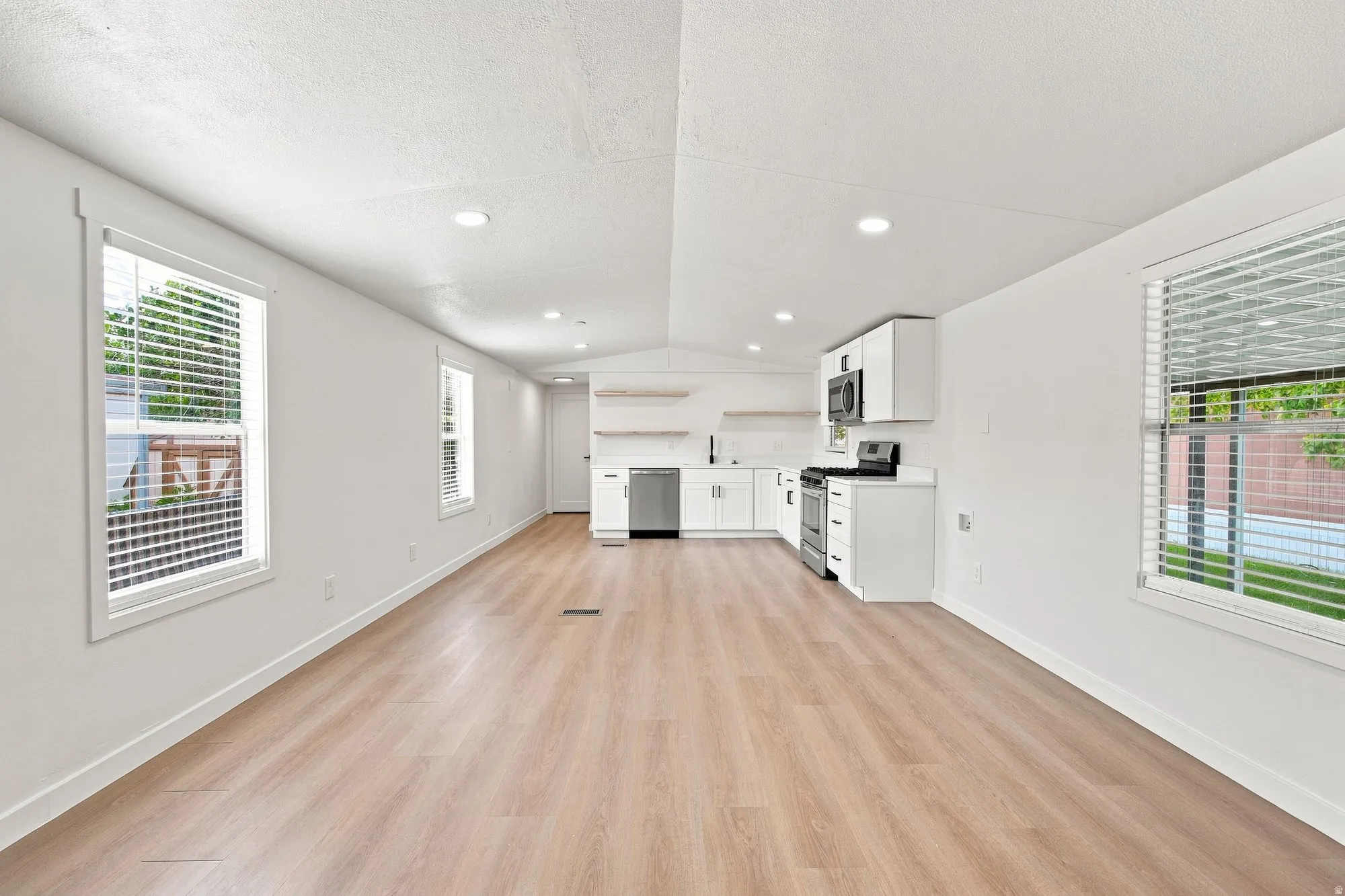 Open-concept living area featuring wood-finish flooring, recessed lighting, and a white kitchen with stainless steel appliances
