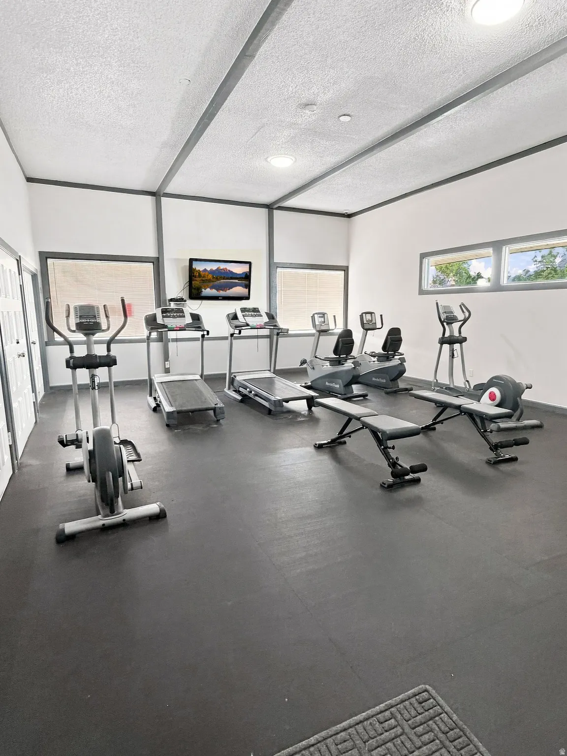 Dedicated fitness room with durable rubber flooring, recessed lighting, and multiple windows