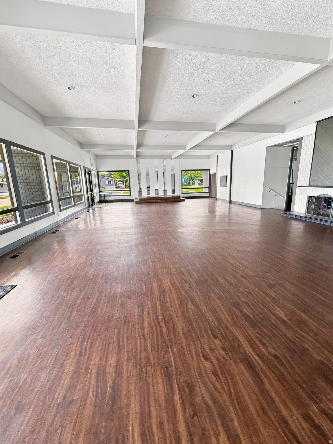 Expansive open-concept room featuring wood-finish flooring, numerous windows, and a coffered ceiling with recessed lighting