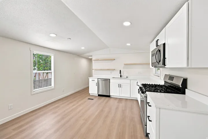 Modern kitchen featuring stainless steel appliances, white cabinetry, integrated sink with matte black fixtures, recessed lighting, and wood-finish flooring