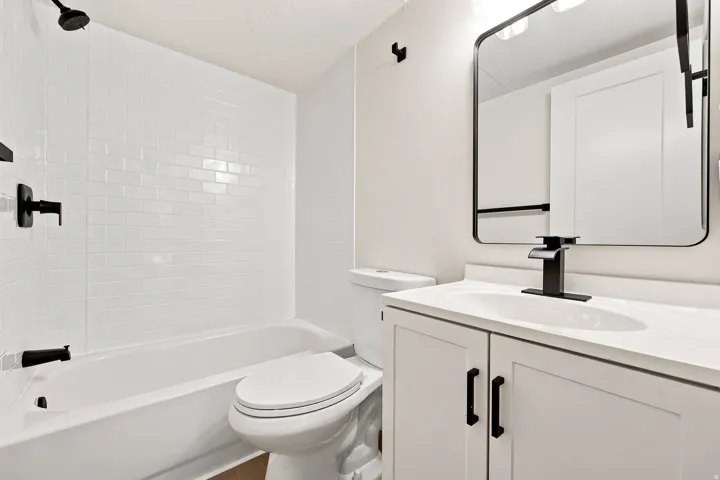 White subway tile surround, matte black fixtures, white vanity with integrated sink, white countertop, and framed mirror