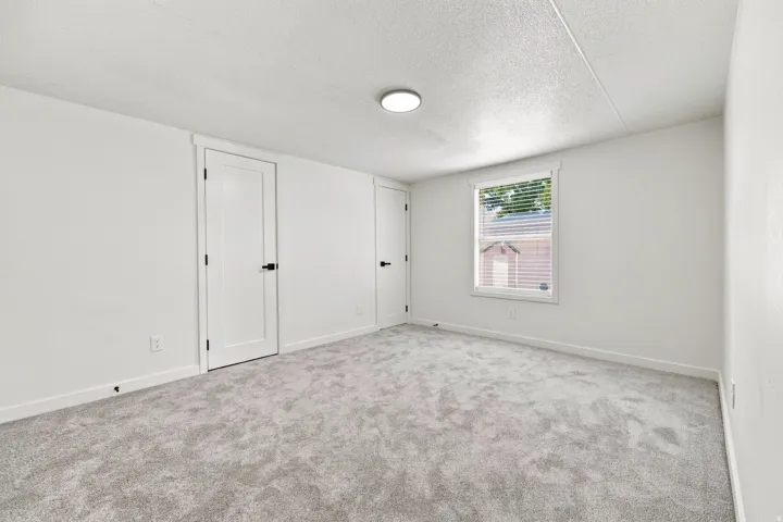 Neutral tone carpeting, white walls, and a window with blinds