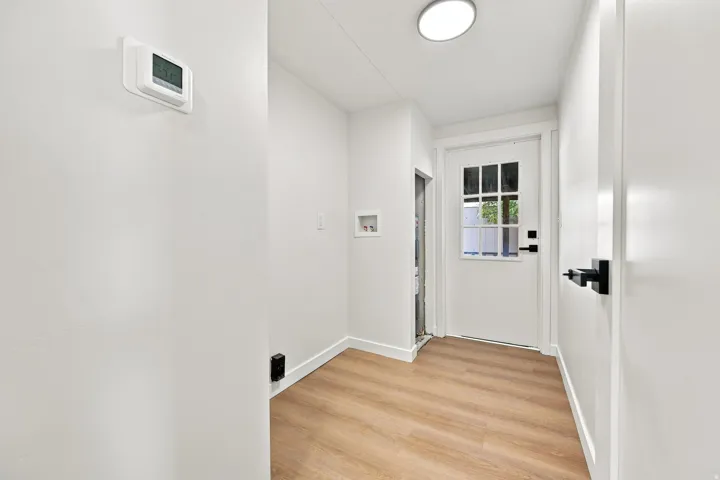 White interior door with windowpanes and black hardware, wood-finish flooring, and recessed ceiling lighting