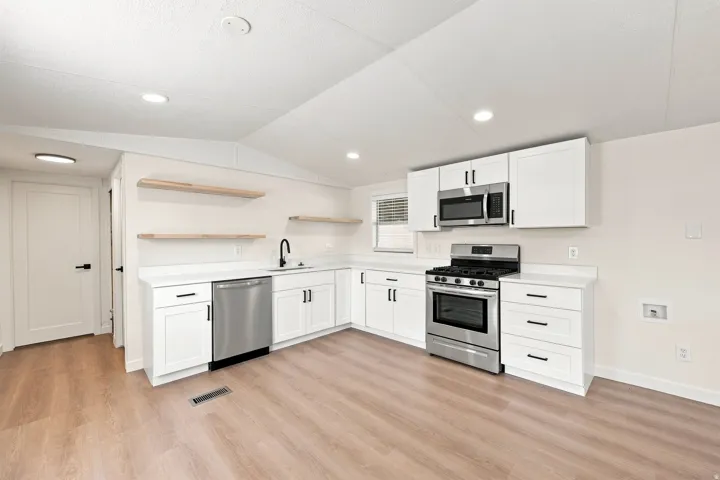 Modern kitchen featuring white cabinetry, stainless steel appliances, light-toned countertops, wood-finish flooring, and open shelving