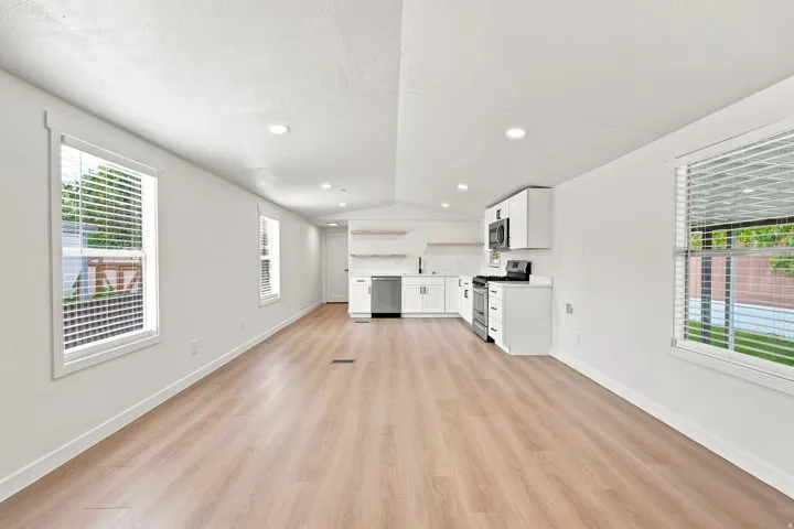 Open-concept living area featuring wood-finish flooring, recessed lighting, and a white kitchen with stainless steel appliances