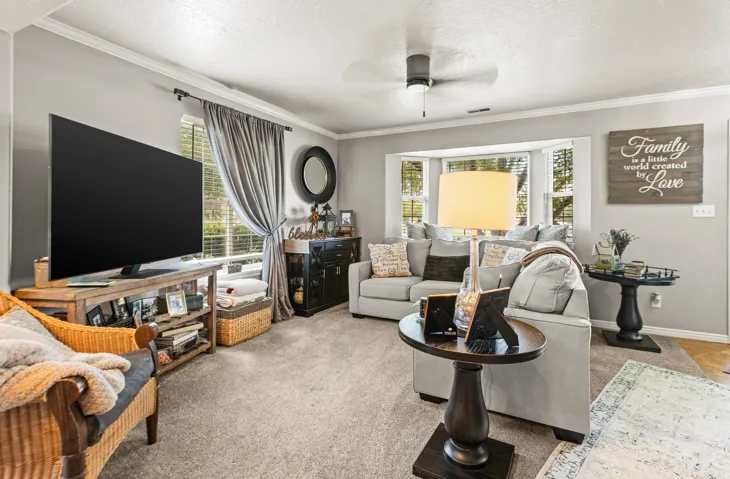 Bay window with multiple panes, ceiling fan, crown molding, and wall-to-wall carpeting