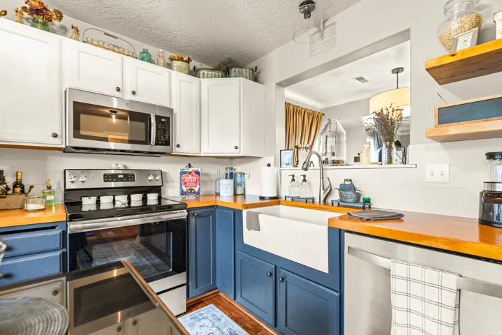 Two-tone cabinetry with wood-finish countertops, stainless steel appliances, and a farmhouse sink