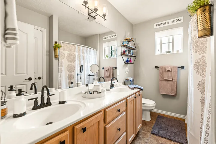 Dual vanity with white undermount sinks and black faucets, light wood-finish cabinetry with black hardware, and a large wall-mounted mirror