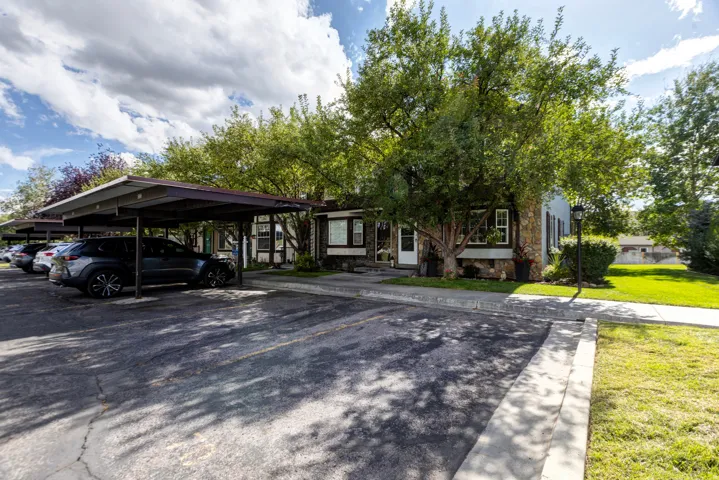 Covered parking structures, mature trees, stone exterior accents, landscaped grass areas, and a concrete pathway