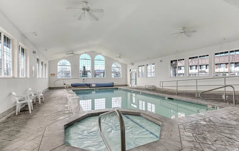 Indoor swimming pool with an integrated spa, vaulted ceiling, and ample natural light from multiple arched and rectangular windows