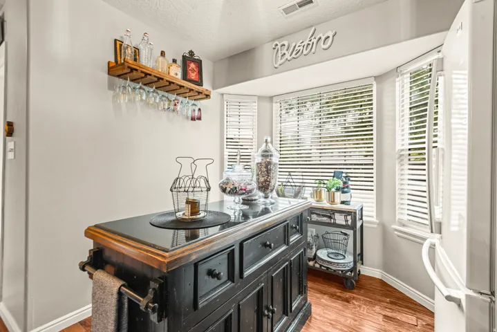 Built-in wood shelving with glass rack, bay window with blinds, wood-finish flooring, and a freestanding kitchen island with drawers