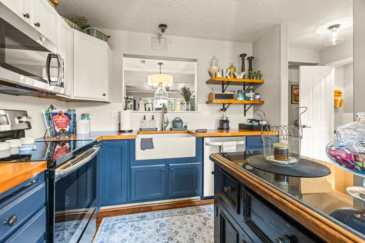 Kitchen featuring wood-finish countertops, contrasting blue and white cabinetry, a large farmhouse sink, stainless steel appliances, and built-in wood shelving