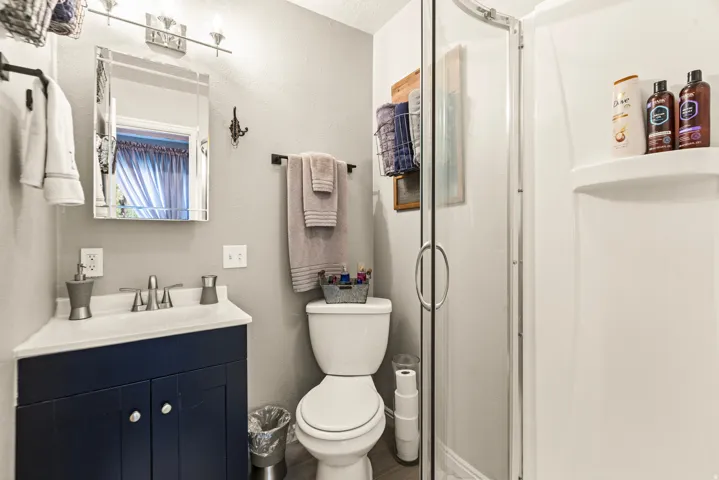 Corner vanity with a white countertop and blue cabinetry, brushed nickel faucet, beveled mirror, and a stand-up shower with a clear glass enclosure