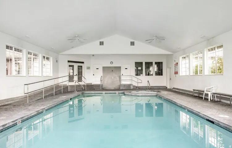 Indoor swimming pool with an integrated spa, vaulted ceiling, multiple windows, and dual ceiling fans