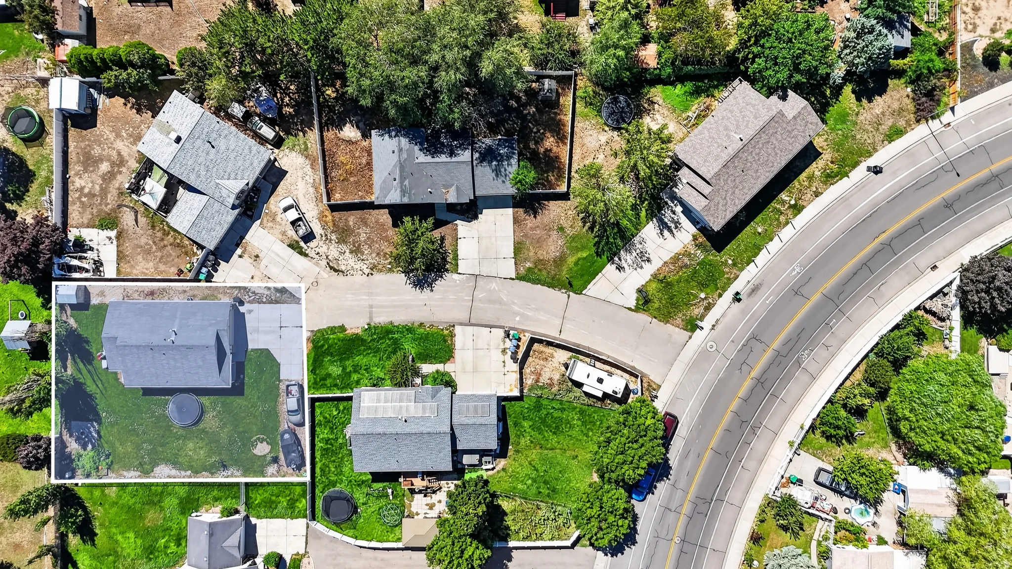 Aerial overview featuring multiple residential properties, established landscaping, and a prominent curved thoroughfare