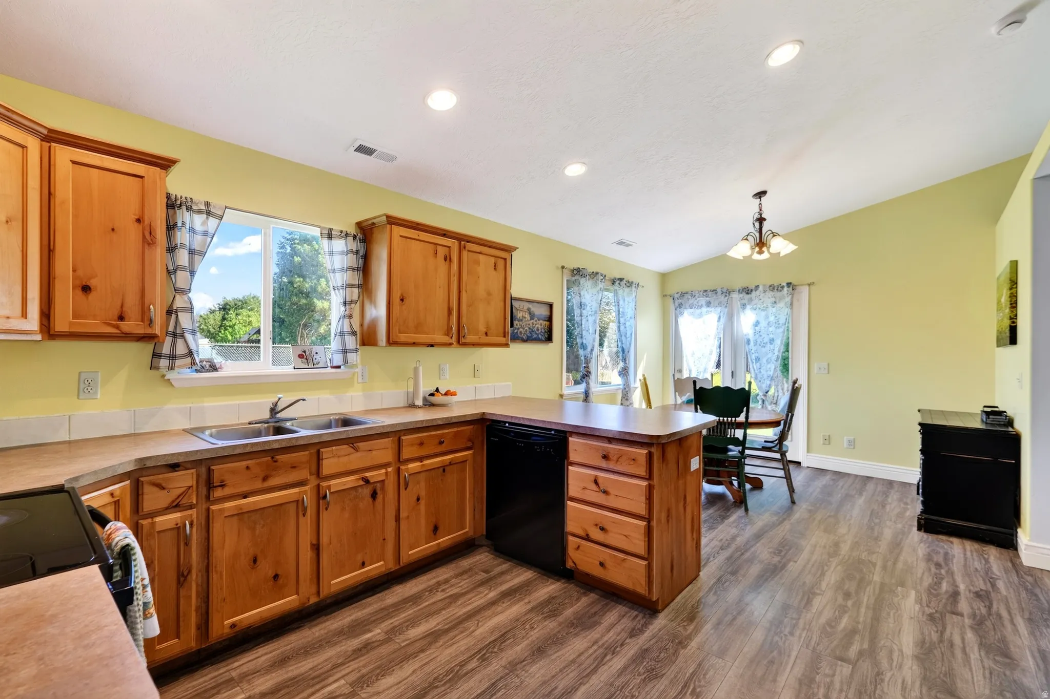 Kitchen featuring wood cabinetry, laminate countertops, a double basin sink, black appliances, and wood-finish flooring