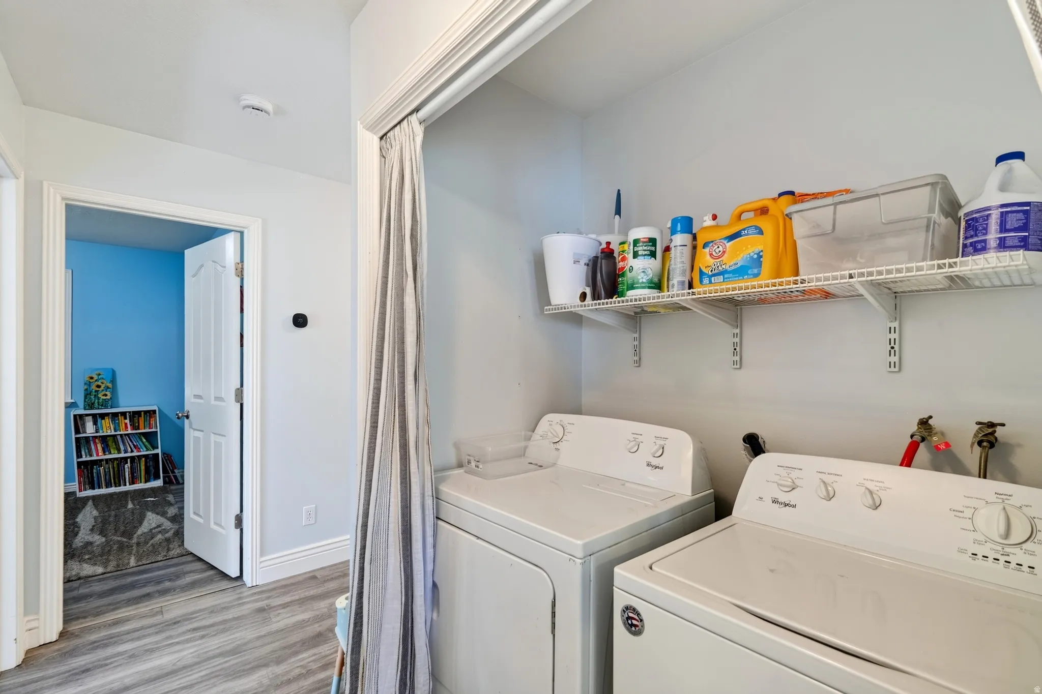 Laundry area with overhead wire shelving, finished flooring, and an adjacent room with a separate flooring material