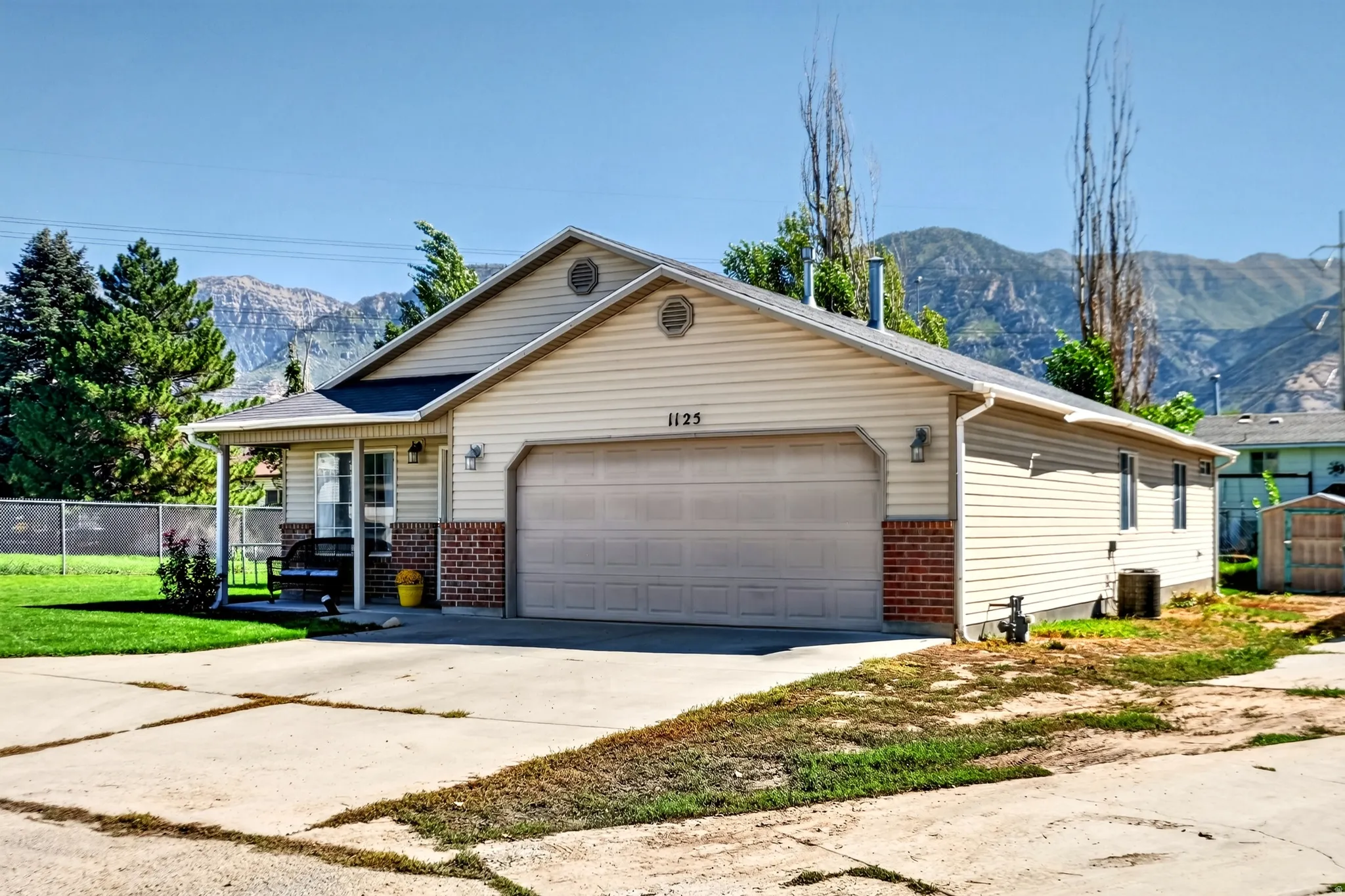 Single-story residence featuring light-colored siding, brick accent detailing, an attached two-car garage, and a covered front entry