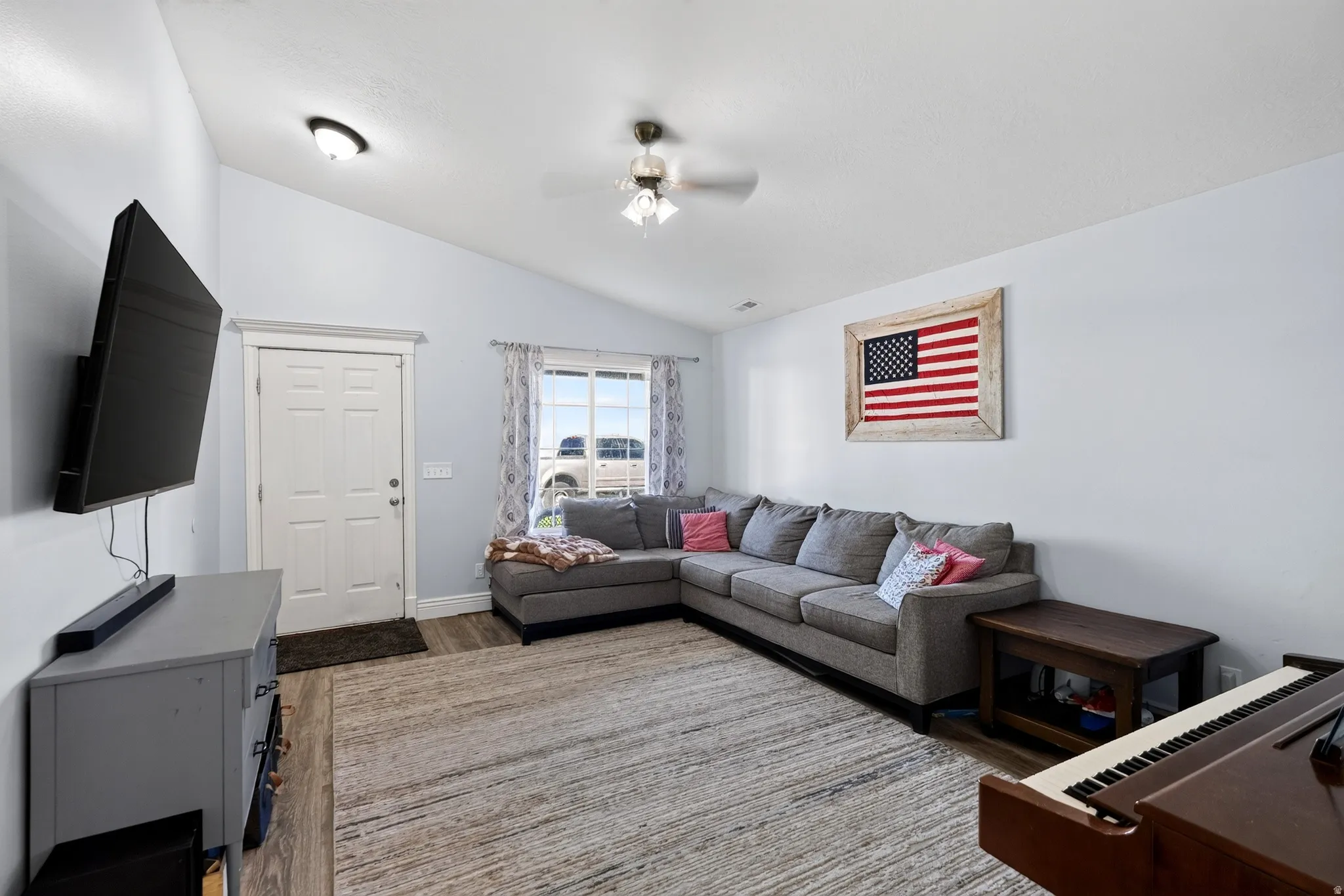 Vaulted ceiling, wood-finish flooring, ceiling fan, paneled door, and window with vertical blinds