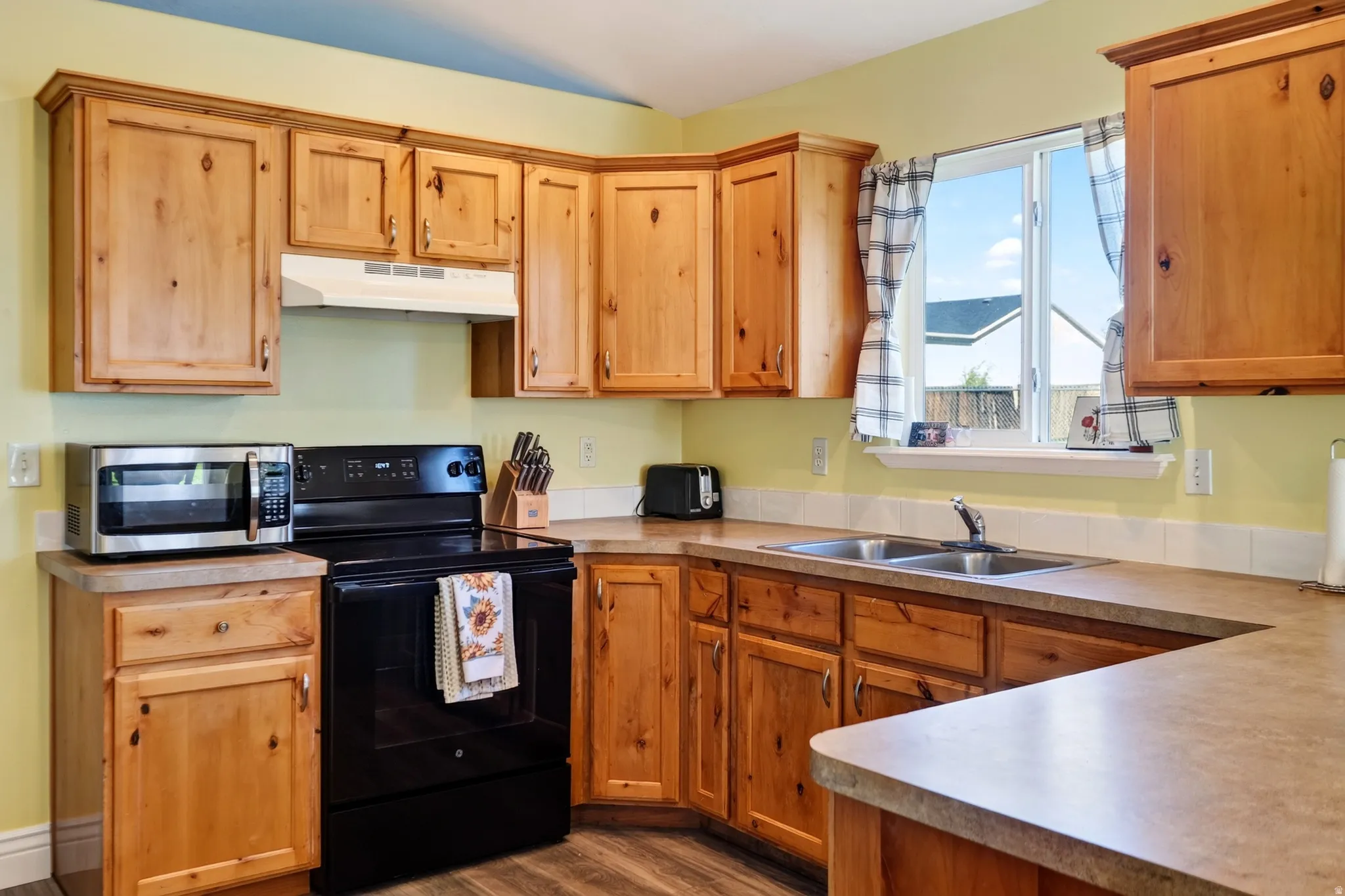 Kitchen featuring warm wood cabinetry, laminate countertops, a double basin stainless steel sink, a black electric range, and a window with natural light