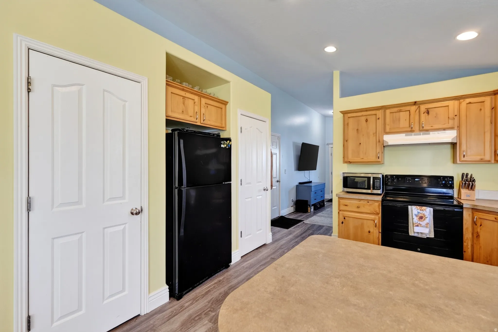 Wood-finish flooring, recessed lighting, wood cabinetry, black refrigerator, and black range