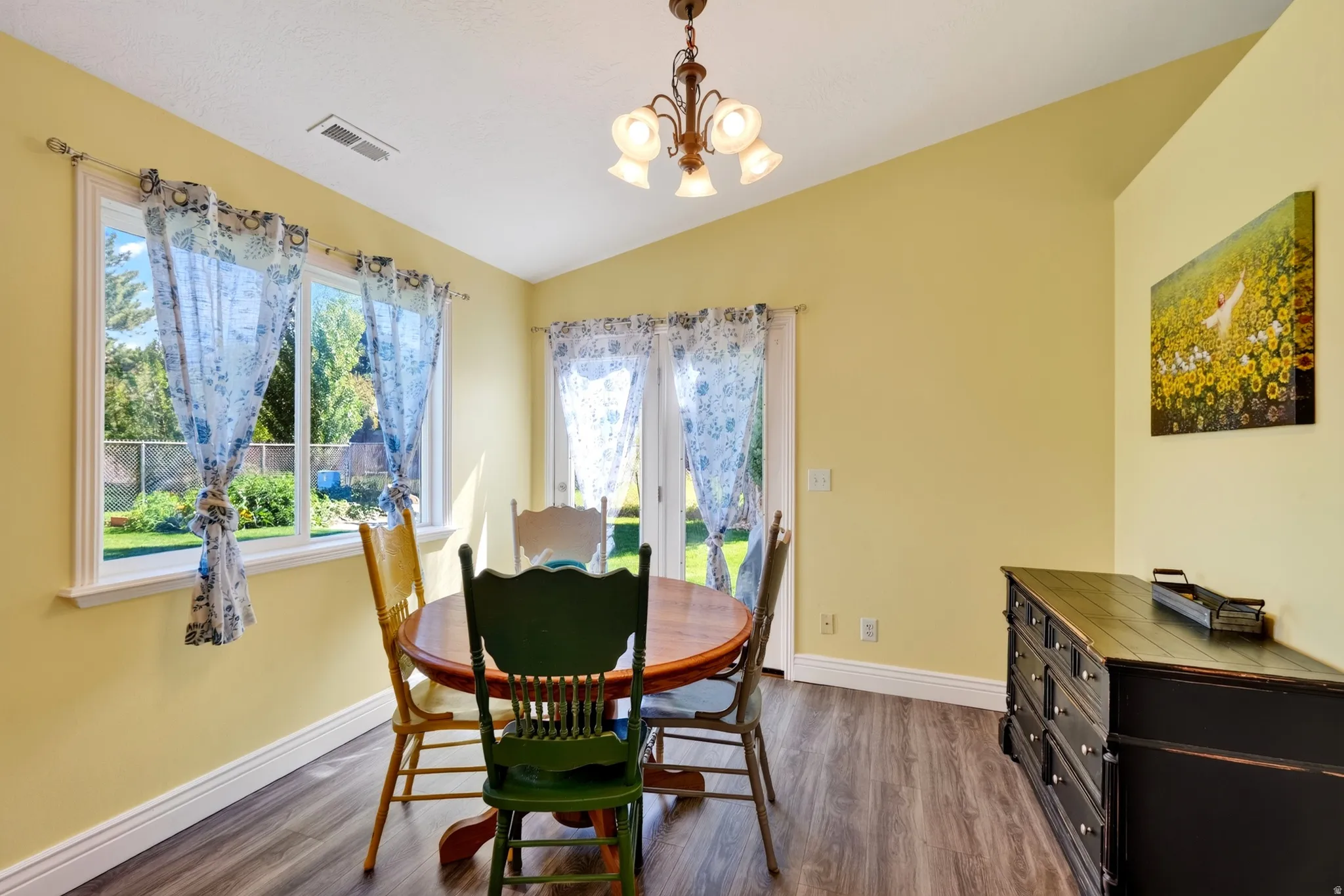 Vaulted ceiling with a chandelier, wood-finish flooring, and a double window