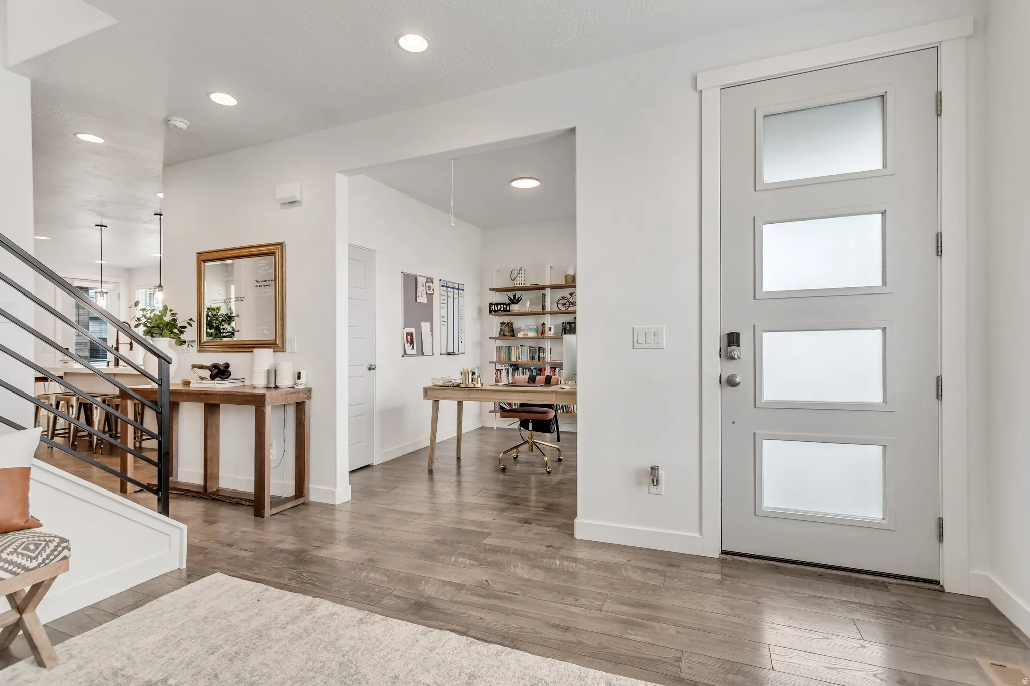 Entry door with four frosted glass panels, wood-finish flooring, recessed lighting, and a modern stair railing