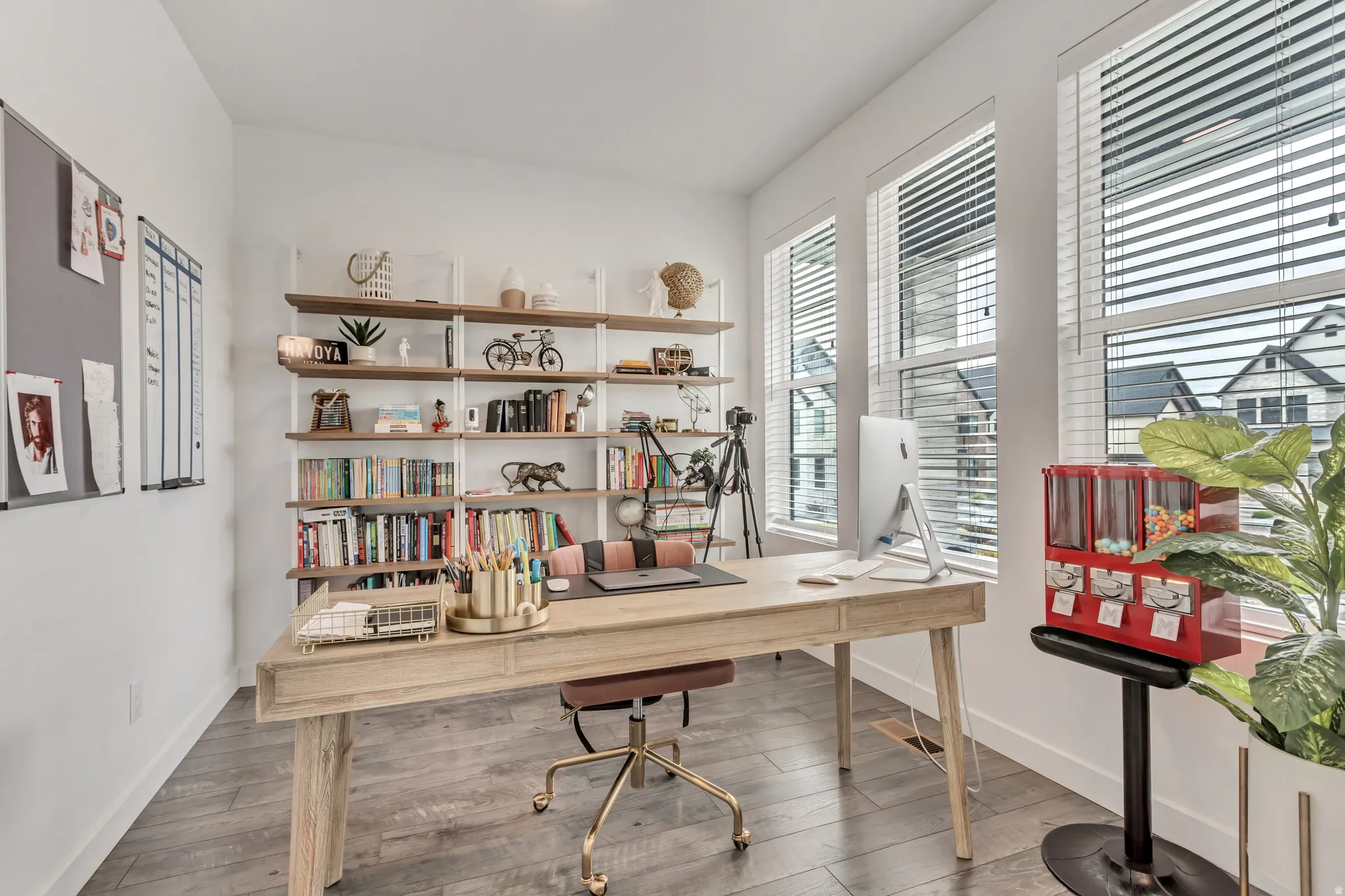 Wide plank wood-finish flooring, white walls, and multiple tall windows with blinds