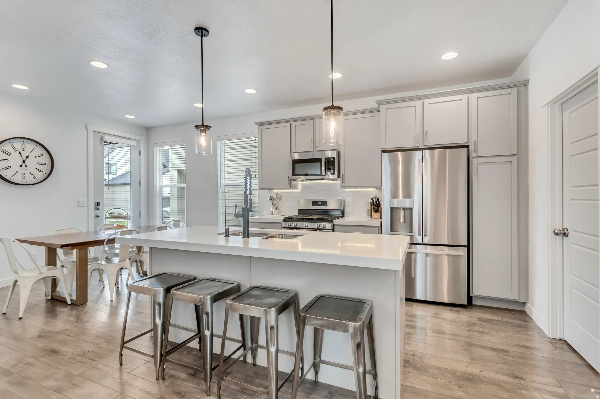 Kitchen featuring a large island with white countertop, gray cabinetry, stainless steel appliances, and wood-finish flooring