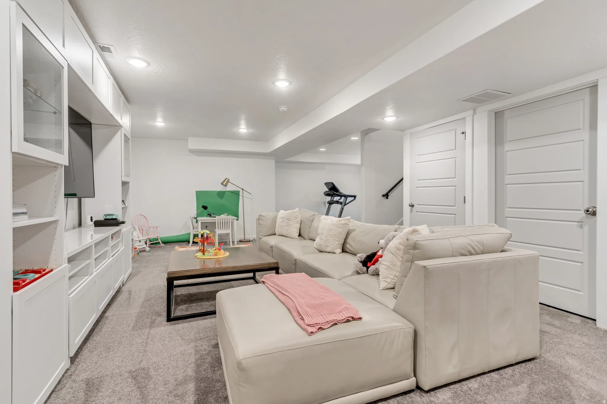 Recessed lighting illuminates a spacious living area featuring a built-in media console with glass-front cabinetry and closed storage