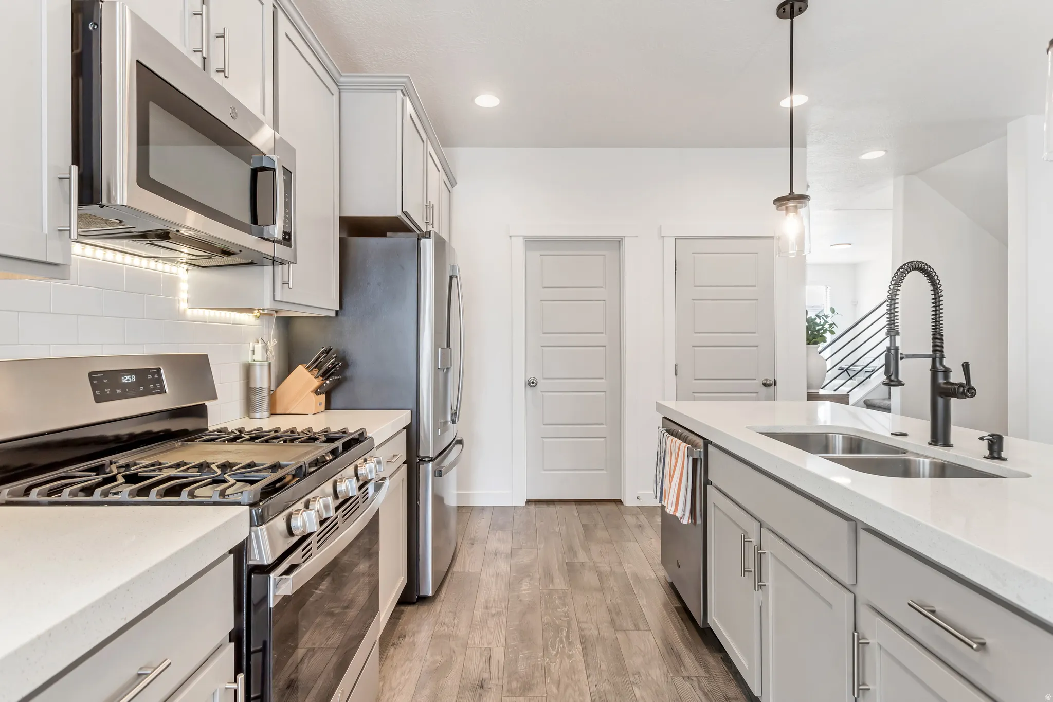 Kitchen featuring stainless steel appliances, light gray cabinetry, white subway tile backsplash, and wood-finish flooring
