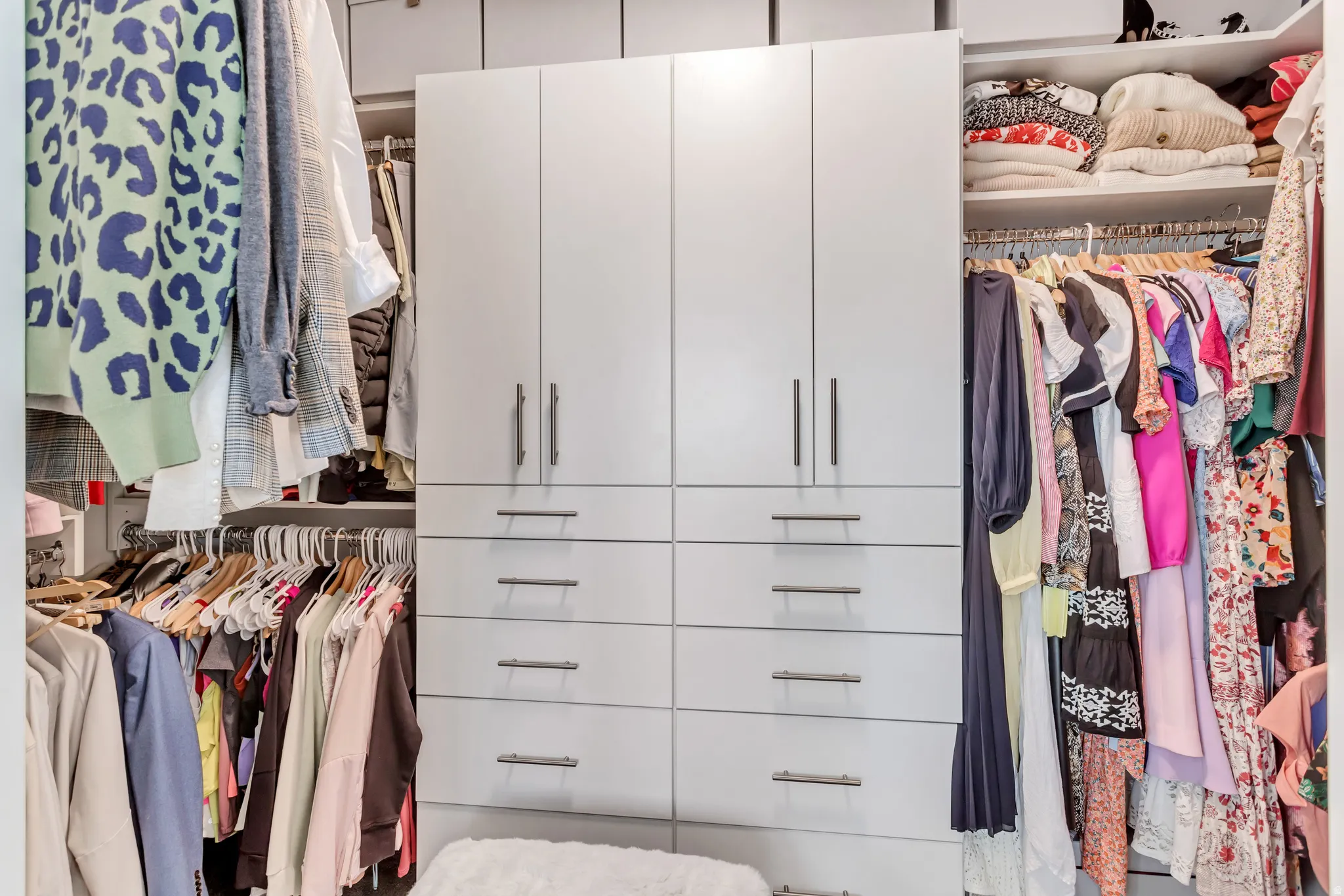 Built-in closet system featuring multiple hanging rods, integrated shelving, and central cabinetry with drawers