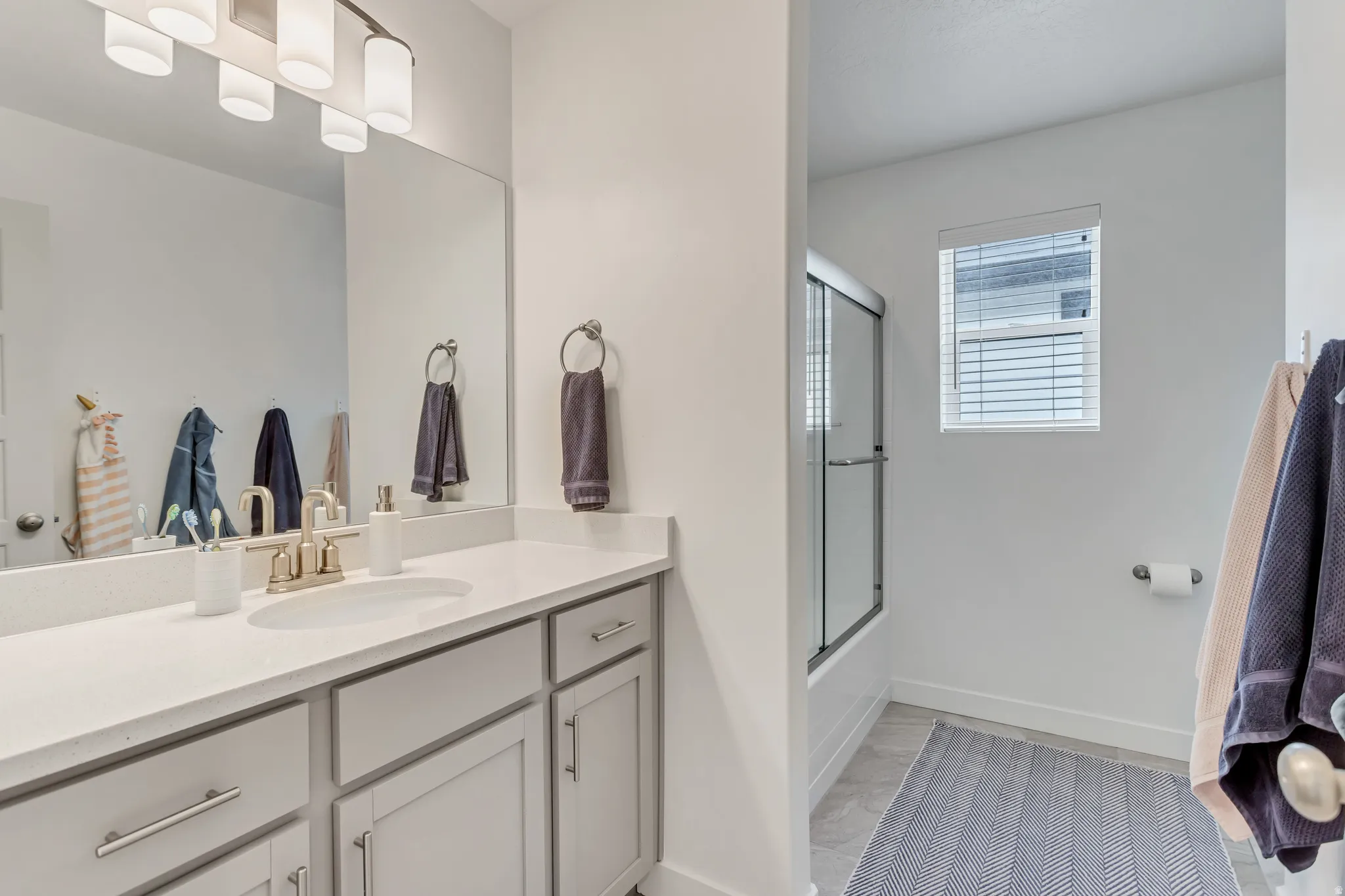Vanity with a single basin sink, light-toned countertop, and light gray cabinetry with brushed nickel hardware