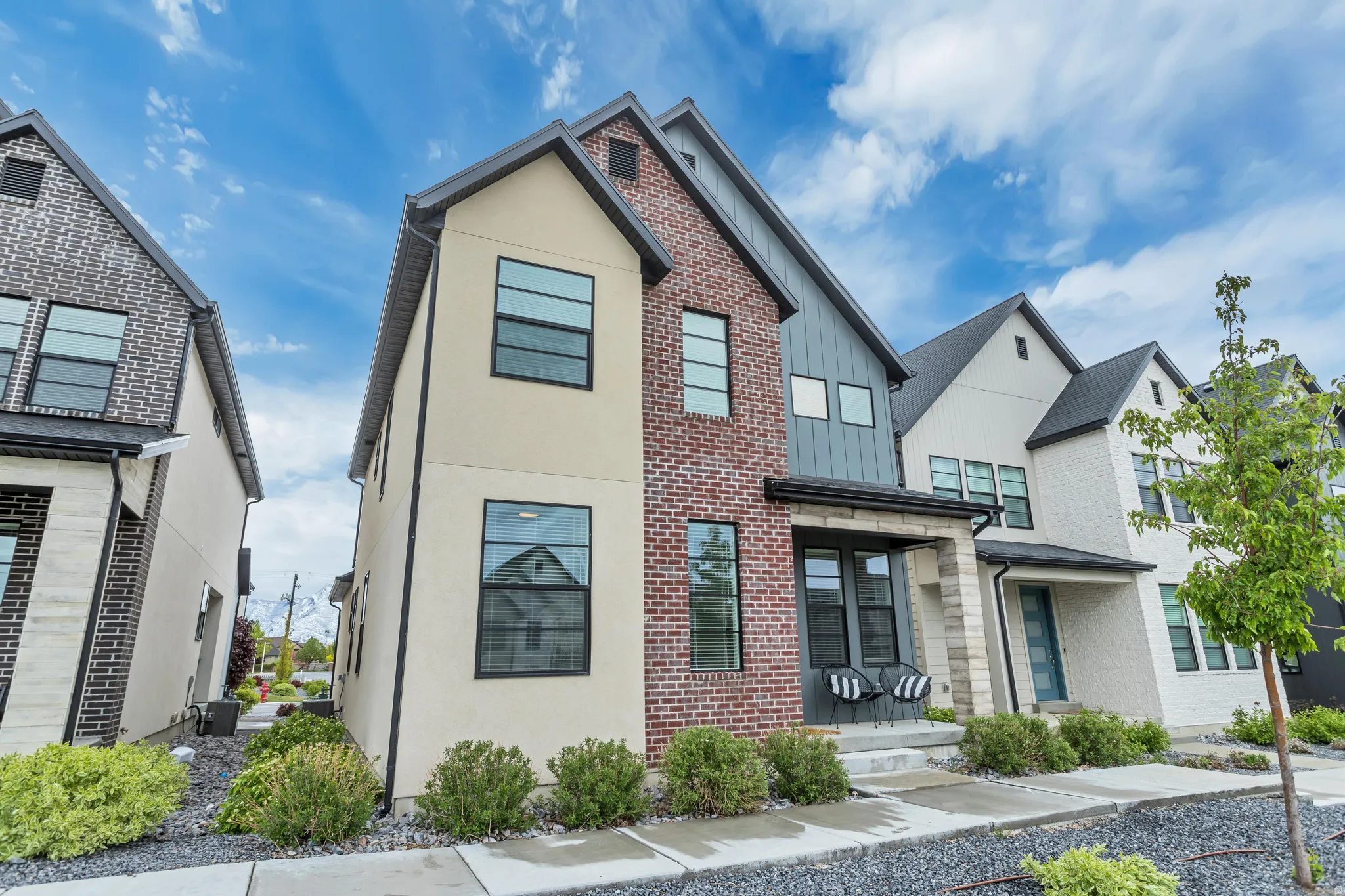 Contemporary multi-story exterior with a mix of brick and stucco finishes, black-framed windows, and a covered entry