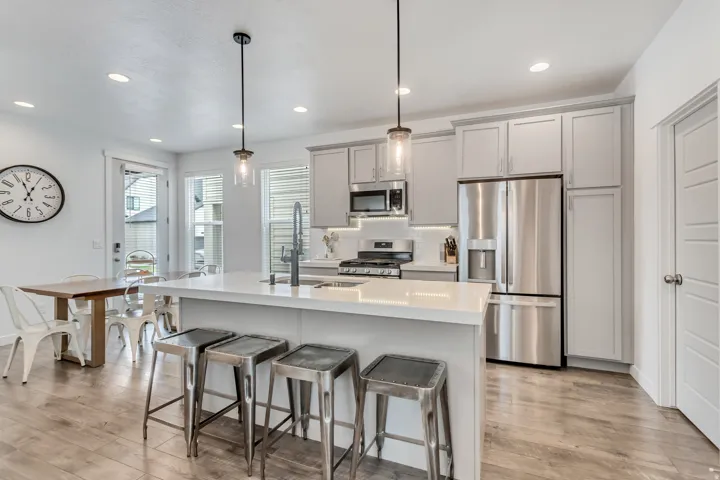 Kitchen featuring a large island with white countertop, gray cabinetry, stainless steel appliances, and wood-finish flooring