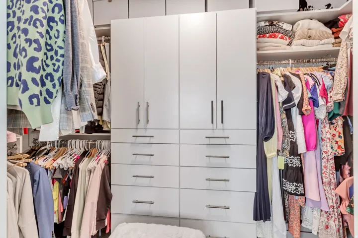 Built-in closet system featuring multiple hanging rods, integrated shelving, and central cabinetry with drawers
