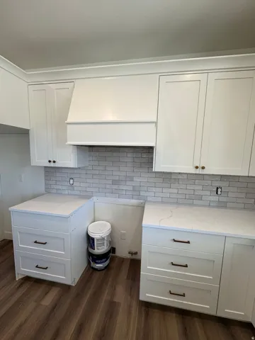 White shaker-style cabinetry, light-toned countertop, subway tile backsplash, white range hood, and wood-finish flooring