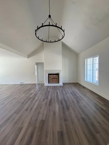 Vaulted ceilings, wood-finish flooring, a white mantel fireplace, and a large multi-pane window