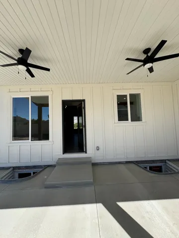 Covered patio featuring two ceiling fans, white board-and-batten siding, and concrete flooring