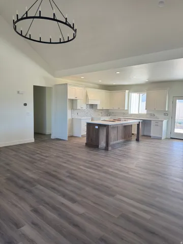 Vaulted ceilings with a circular chandelier, wood-finish flooring, recessed lighting, and a kitchen featuring white cabinetry, a wood-finish island, and light-toned countertops