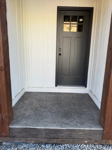 Craftsman-style entry door with divided lites, board-and-batten siding, and a textured concrete entry pad