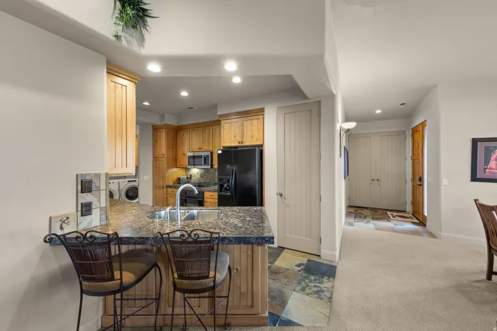 Kitchen featuring wood cabinetry, stainless steel sink, black appliances, and granite-style countertops